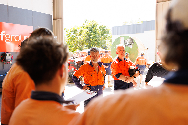 A group of men in orange shirts engaged in conversation, representing Huffgroup Electrical Services