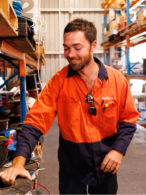 A man in an orange shirt and blue jeans works on a machine at Huffgroup electrical
