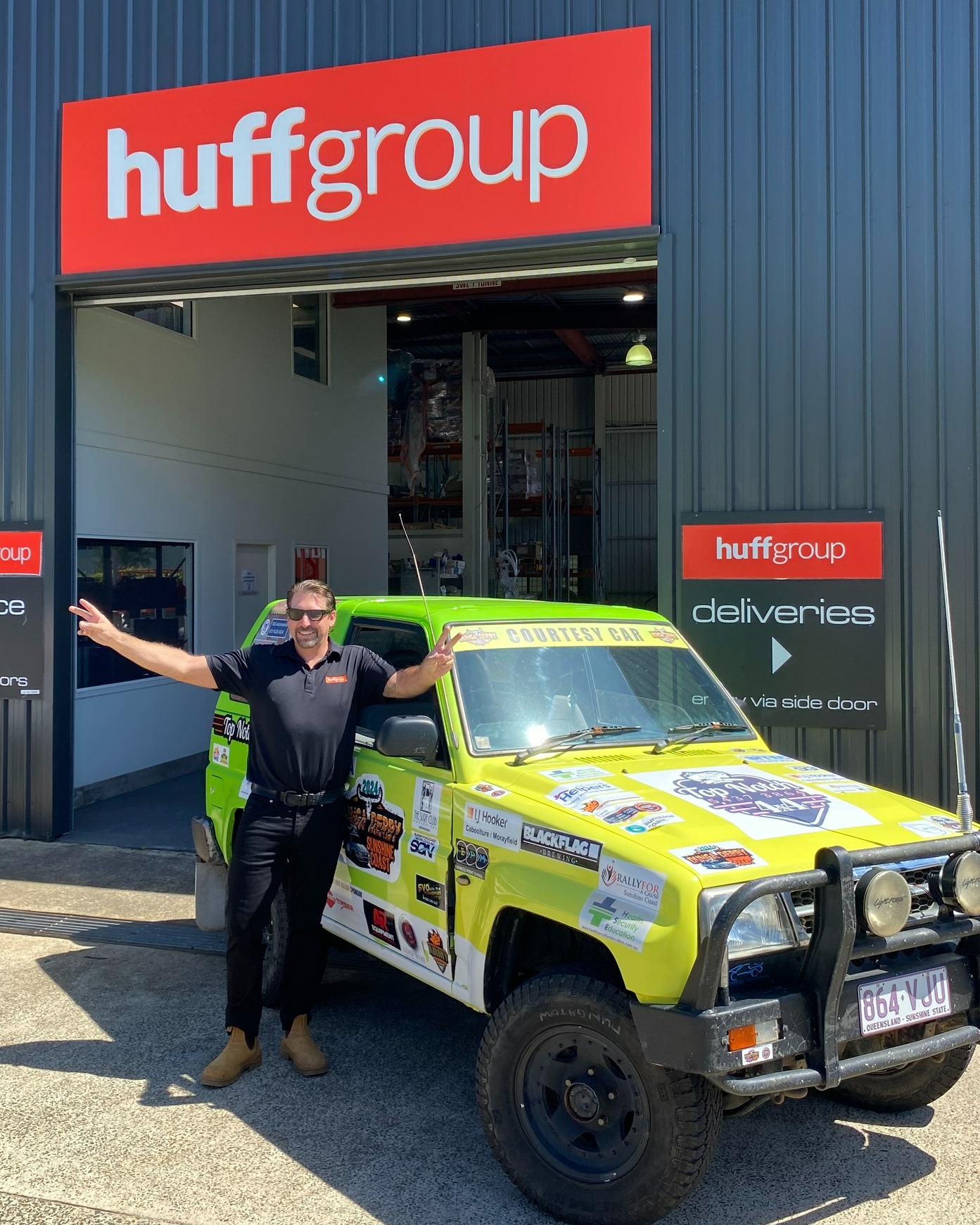 A man stands beside a yellow jeep in front of the Huff Group building, which focuses on community and environmental initiatives