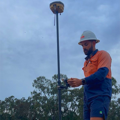 A man wearing an orange shirt and blue pants stands next to a pole, associated with Huff Group - Civil Electrical Service