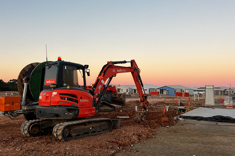 A red excavator is actively working at a construction site, representing Huff Group - Plant, Equipment, and Facilities