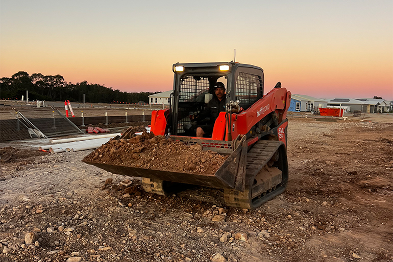 A small red skid steer loader parked on a dirt lot, labeled with "Huff Group - Plant, Equipment, and Facilities